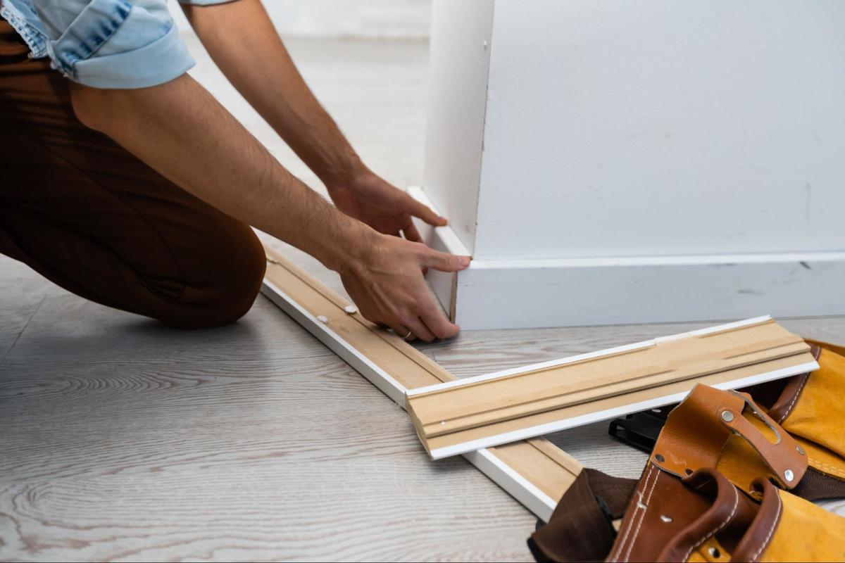 Vakman plaatst plinten in de hoek van een kamer ter afwerking van de laminaatvloer